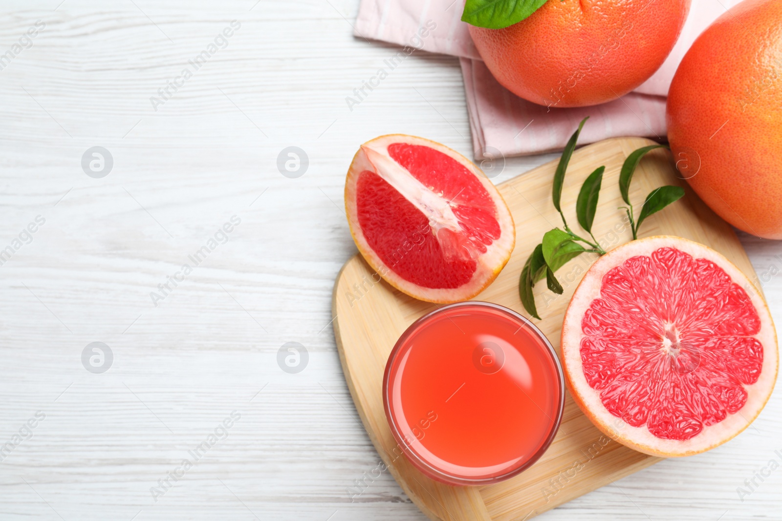 Photo of Tasty freshly made grapefruit juice and fruits on white wooden table, flat lay. Space for text