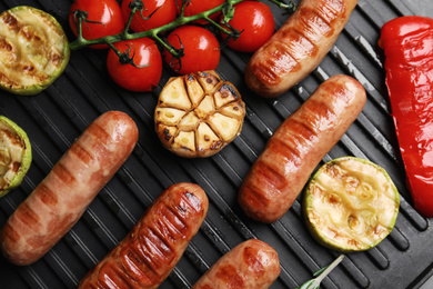 Photo of Cooking delicious fresh sausages with vegetables on modern grill, flat lay