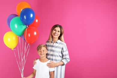 Mother and son with balloons on color background