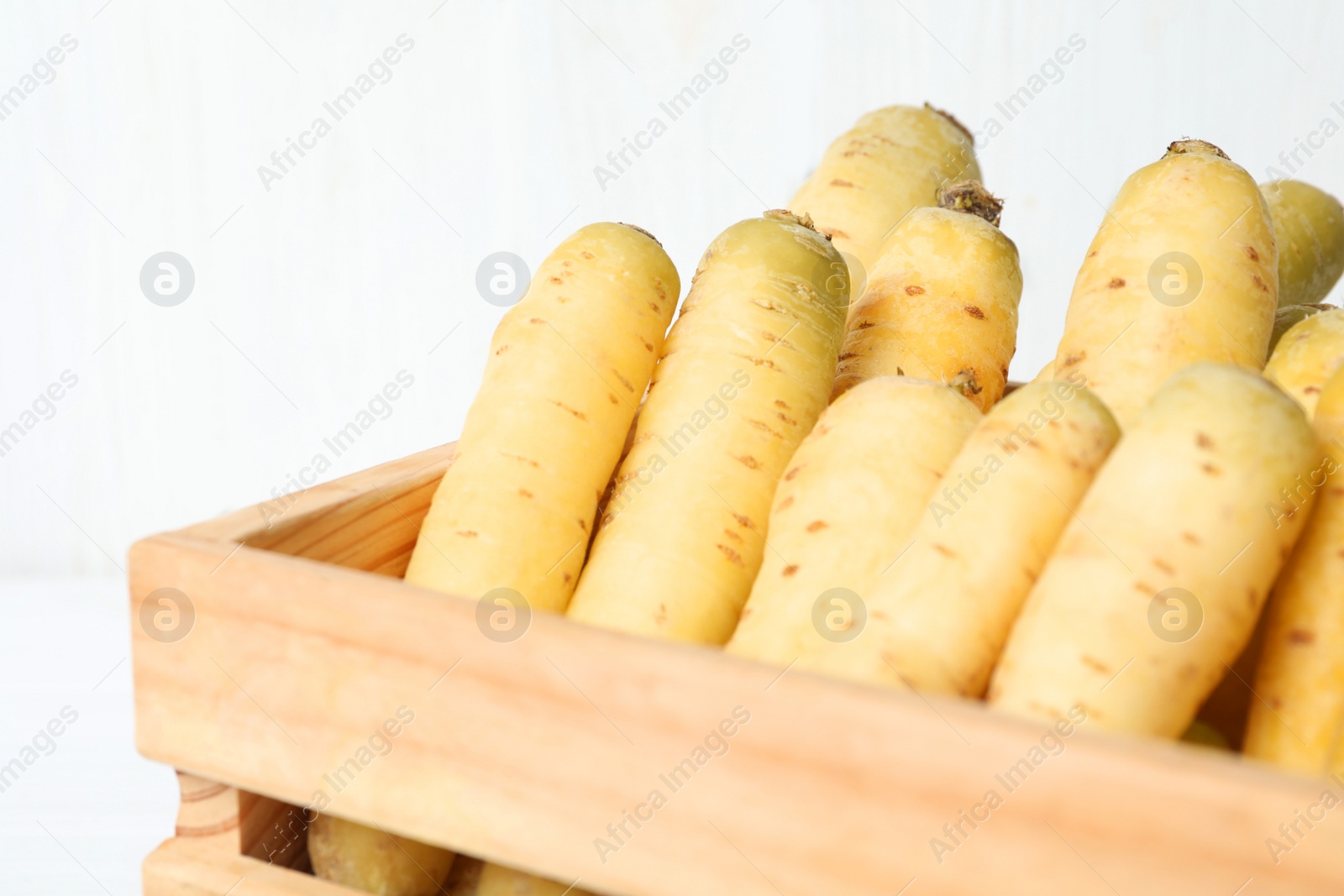 Photo of Raw white carrots in wooden crate, closeup