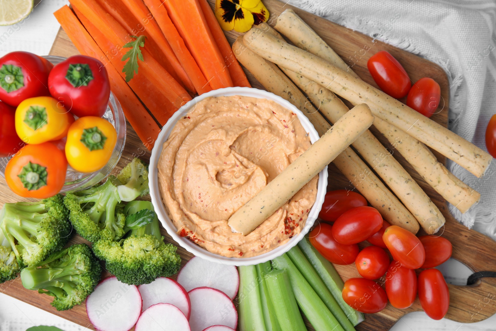 Photo of Board with delicious hummus, grissini sticks and fresh vegetables on white background, flat lay