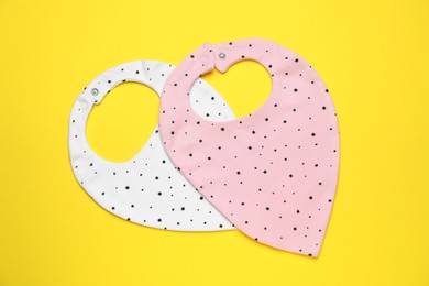 Photo of Two baby bibs on yellow background, top view. First food