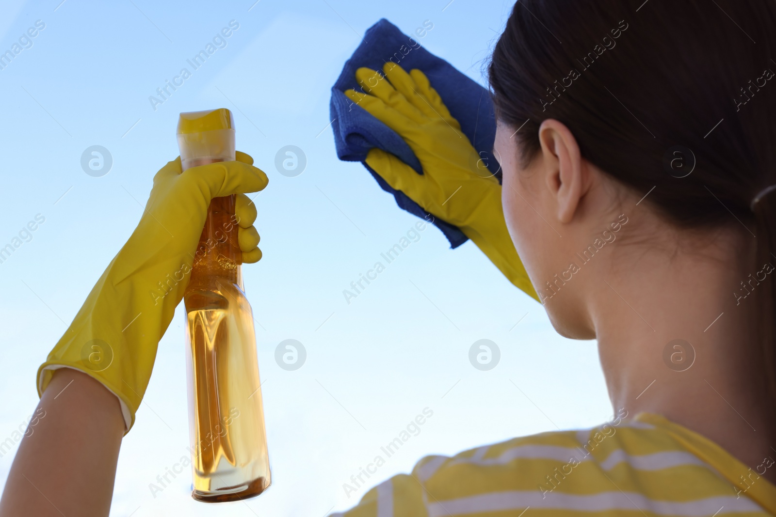Photo of Woman cleaning window glass with rag and detergent, closeup
