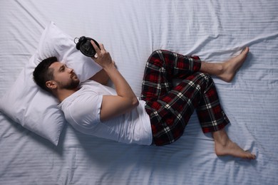 Photo of Man looking at alarm clock on bed, top view. Insomnia problem