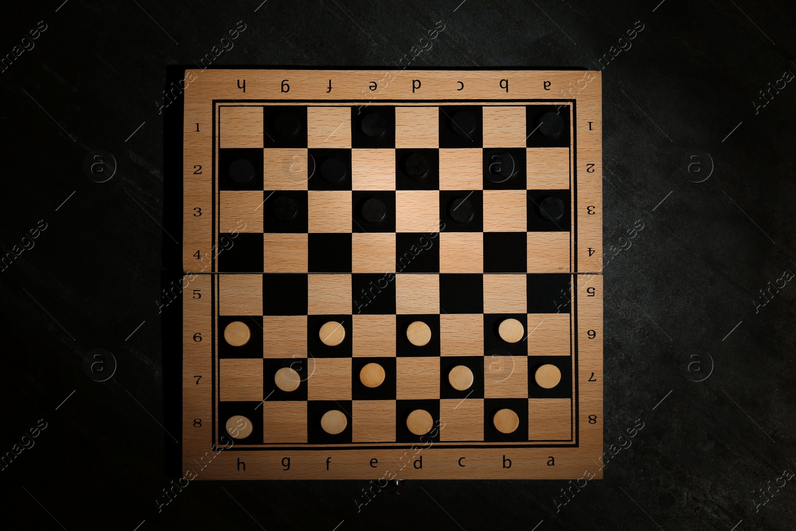 Photo of Wooden checkerboard with game pieces on black table, top view