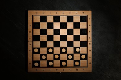 Photo of Wooden checkerboard with game pieces on black table, top view