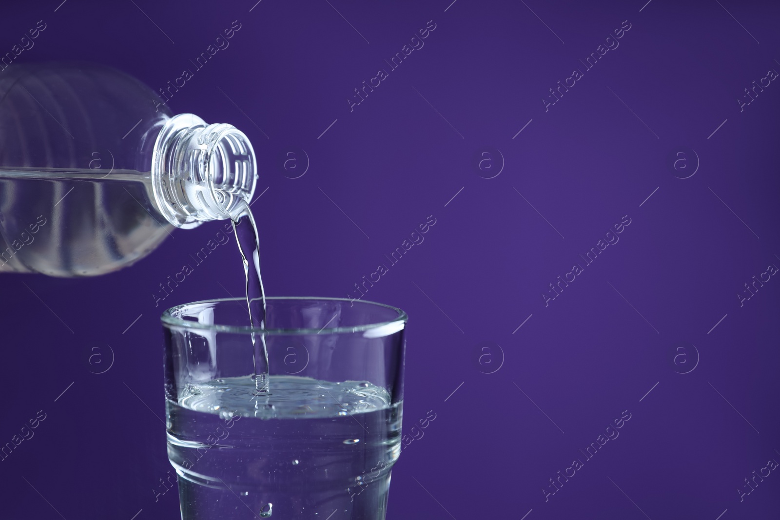 Photo of Pouring water from bottle into glass on purple background, closeup. Space for text