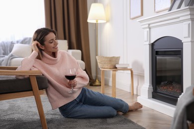 Photo of Young woman with glass of wine resting near fireplace at home