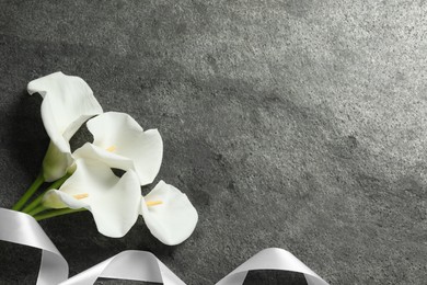 Photo of Beautiful calla lily flowers and white ribbon on grey table, flat lay with space for text. Funeral symbols
