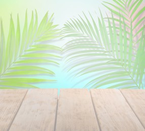 Palm branches and wooden table against color background, fade effect. Summer party