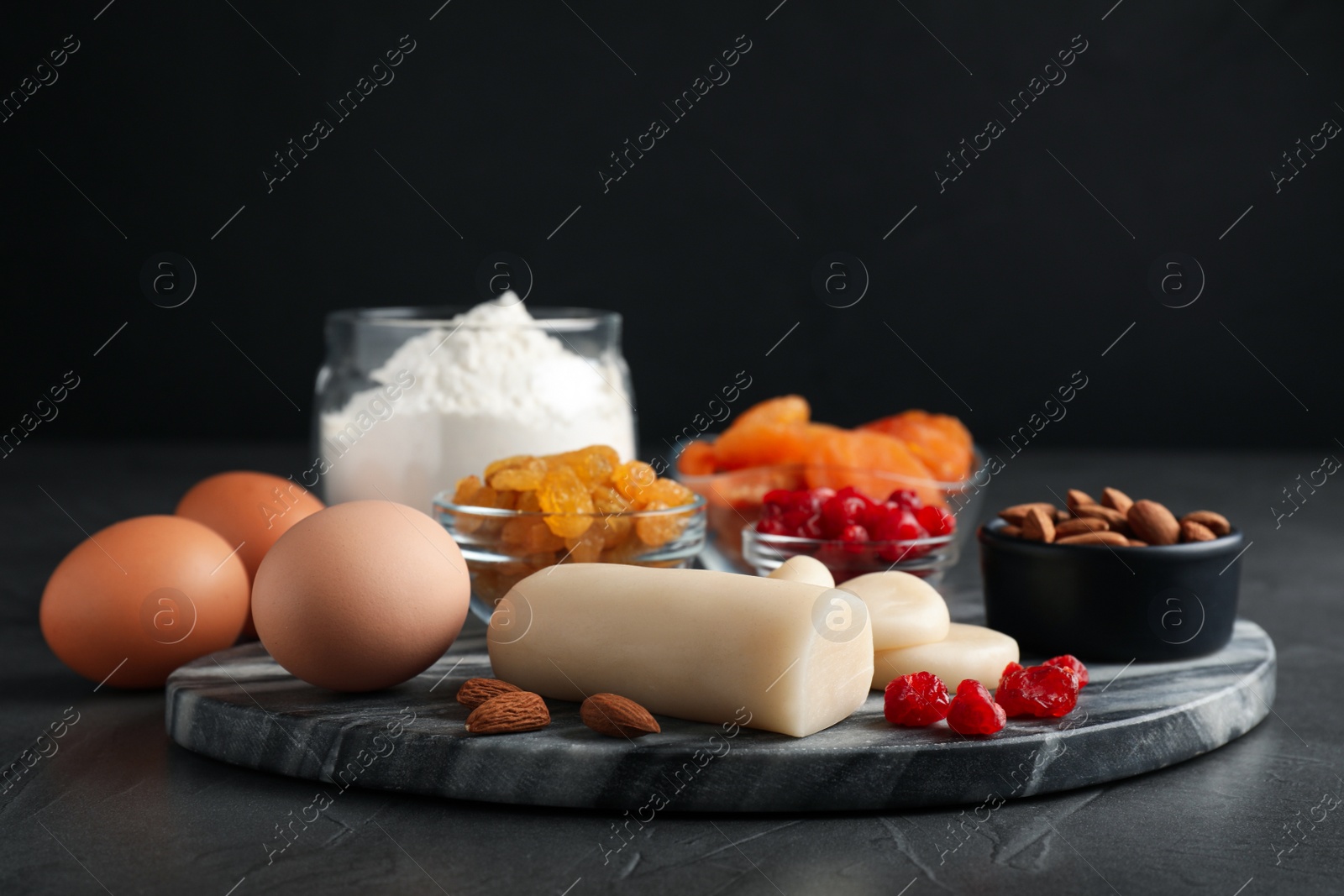 Photo of Marzipan and other ingredients for homemade Stollen on grey table against dark background. Baking traditional German Christmas bread
