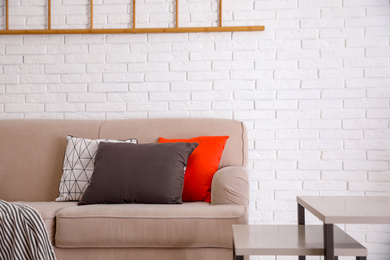 Soft pillows on sofa near white brick wall