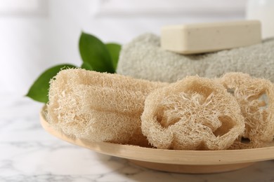 Loofah sponges, soap, towel and green leaves on white marble table, closeup