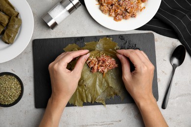 Photo of Top view of woman preparing stuffed grape leaves at light table, closeup