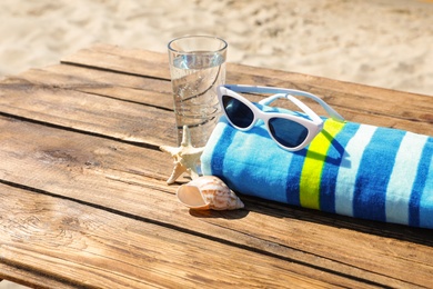 Wooden deck with glass of refreshing drink and beach accessories on hot summer day