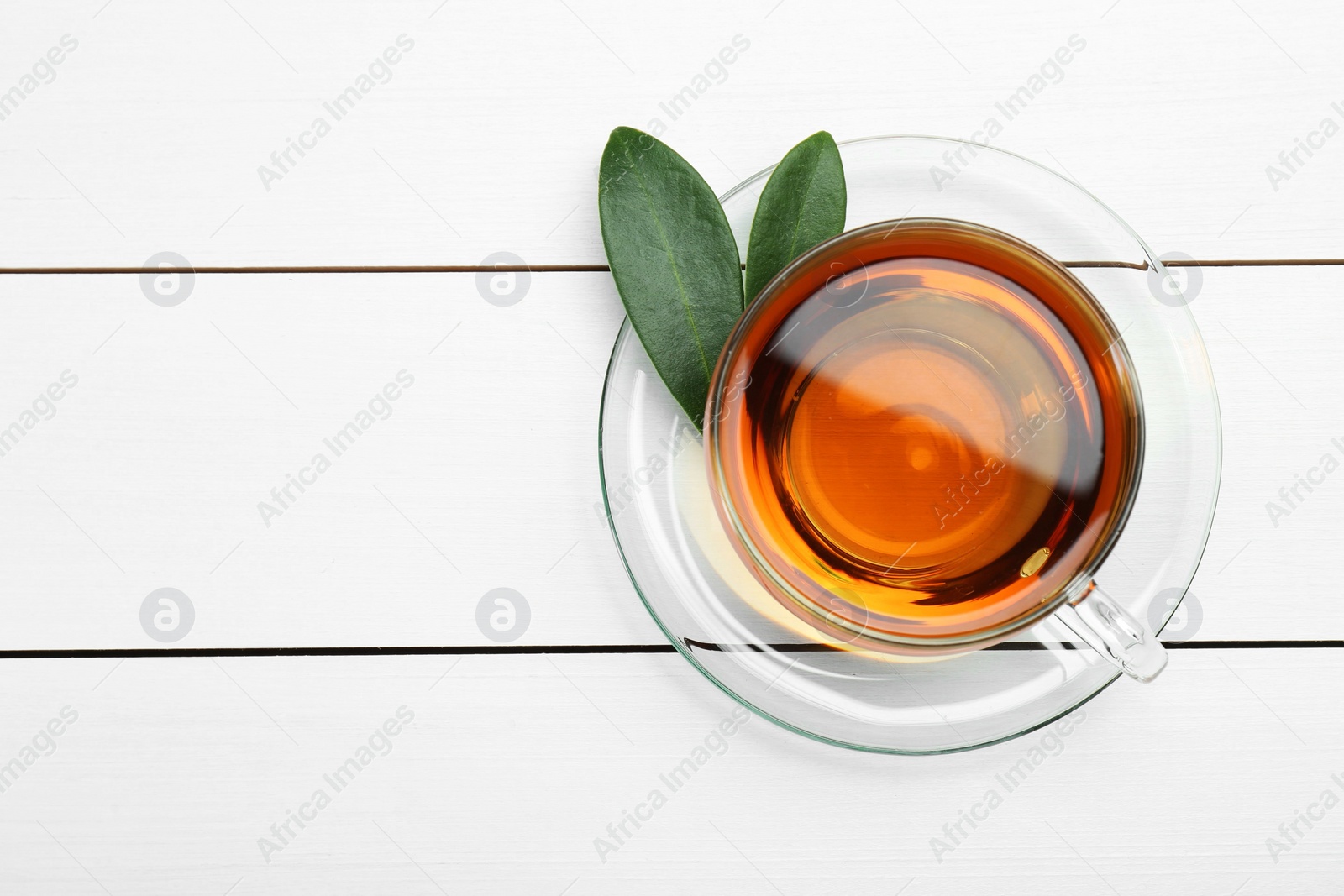 Photo of Aromatic tea in glass cup and green leaves on white wooden table, top view. Space for text