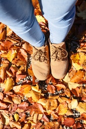 Woman standing on ground covered with fallen autumn leaves, top view