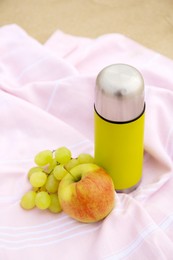 Photo of Metallic thermos with hot drink and fruits on plaid outdoors