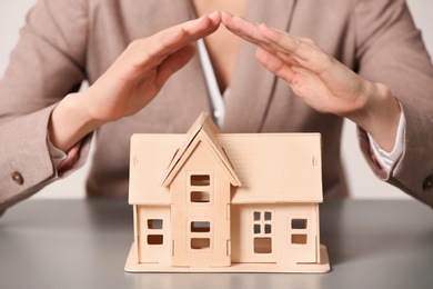 Photo of Female agent covering house model at table, closeup. Home insurance