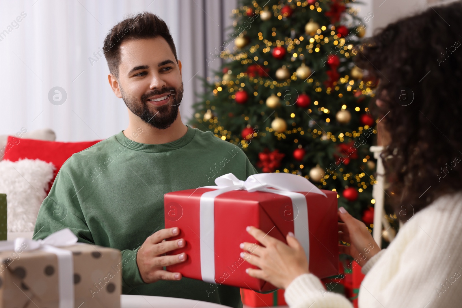 Photo of Christmas celebration. Woman and man exchanging gifts at home