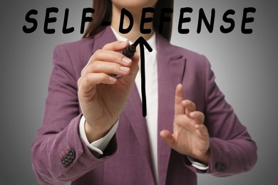 Image of Self defense. Woman drawing arrow with marker on glass board against grey background, closeup