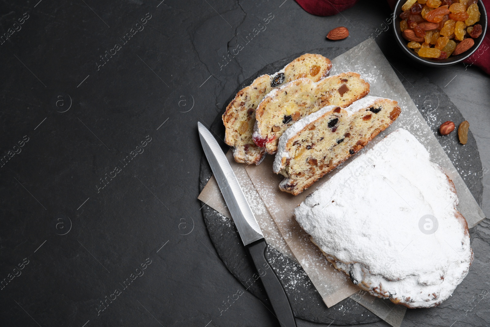 Photo of Traditional Christmas Stollen with icing sugar on black table, flat lay. Space for text