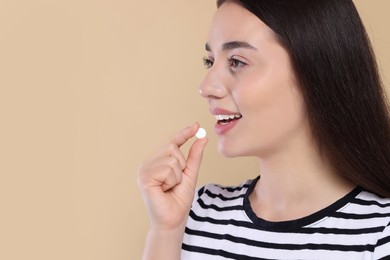 Happy woman taking pill on beige background, space for text