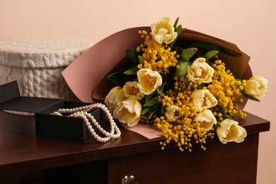 Photo of Bouquet with beautiful spring flowers and necklace on wooden chest of drawers