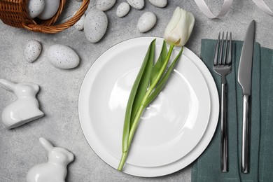 Photo of Festive table setting with painted eggs and white tulip on light grey background, flat lay. Easter celebration