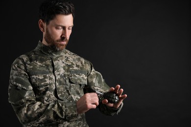 Soldier pulling safety pin out of hand grenade on black background, space for text. Military service