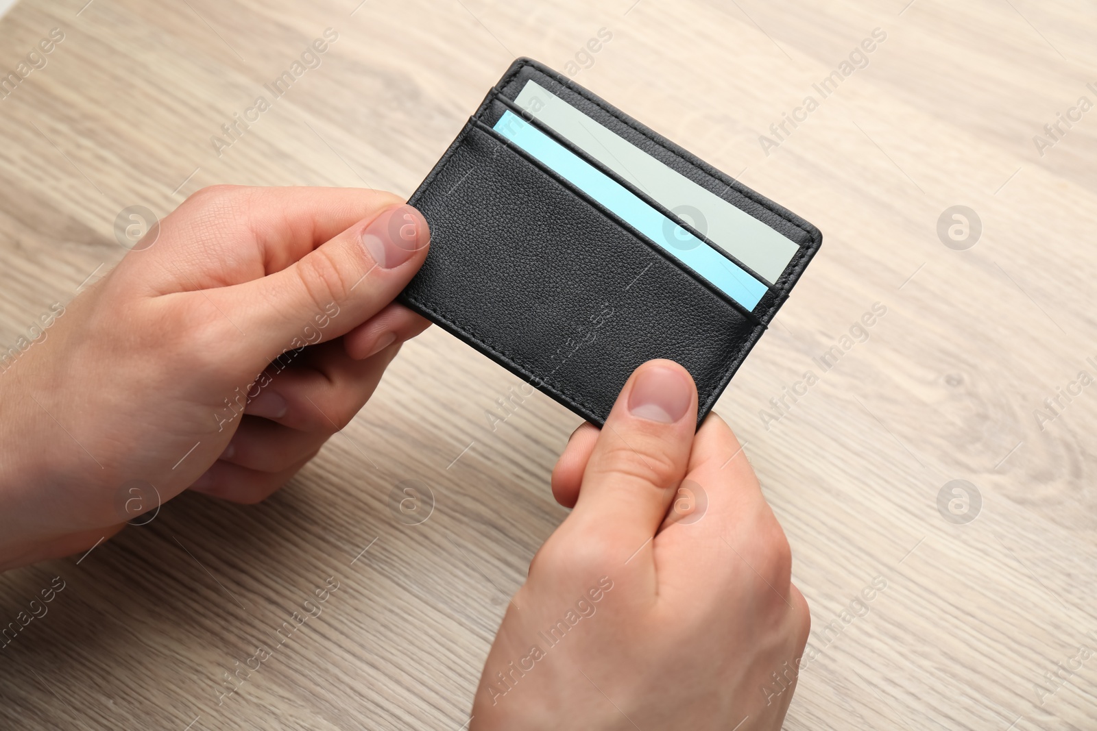 Photo of Man holding leather business card holder with cards at wooden table, closeup