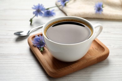 Photo of Cup of delicious chicory drink and flowers on white wooden table, closeup