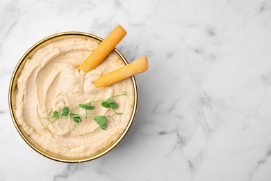 Delicious hummus with grissini sticks on white marble table, top view. Space for text