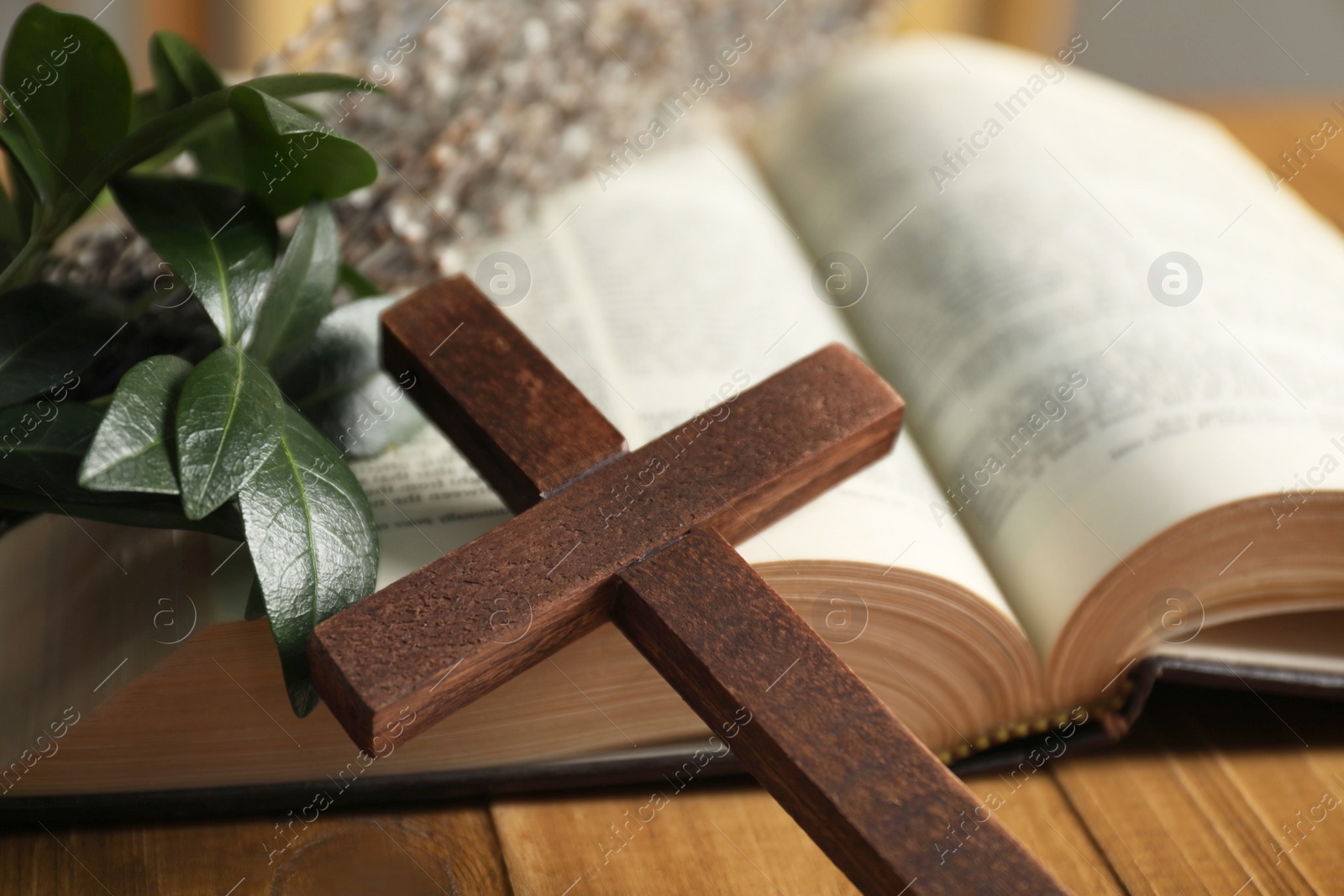 Photo of Cross, Bible and green leaves on table, closeup