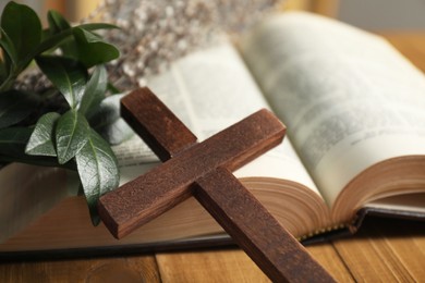 Photo of Cross, Bible and green leaves on table, closeup