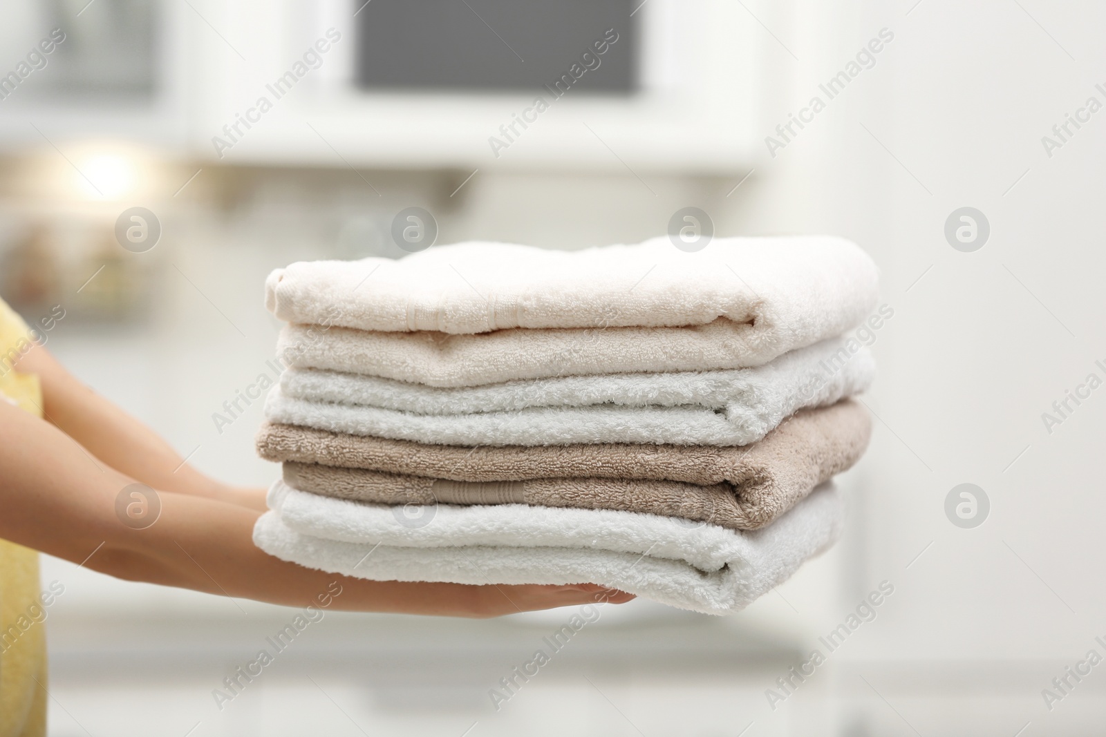 Photo of Woman holding folded clean towels in kitchen, closeup. Laundry day