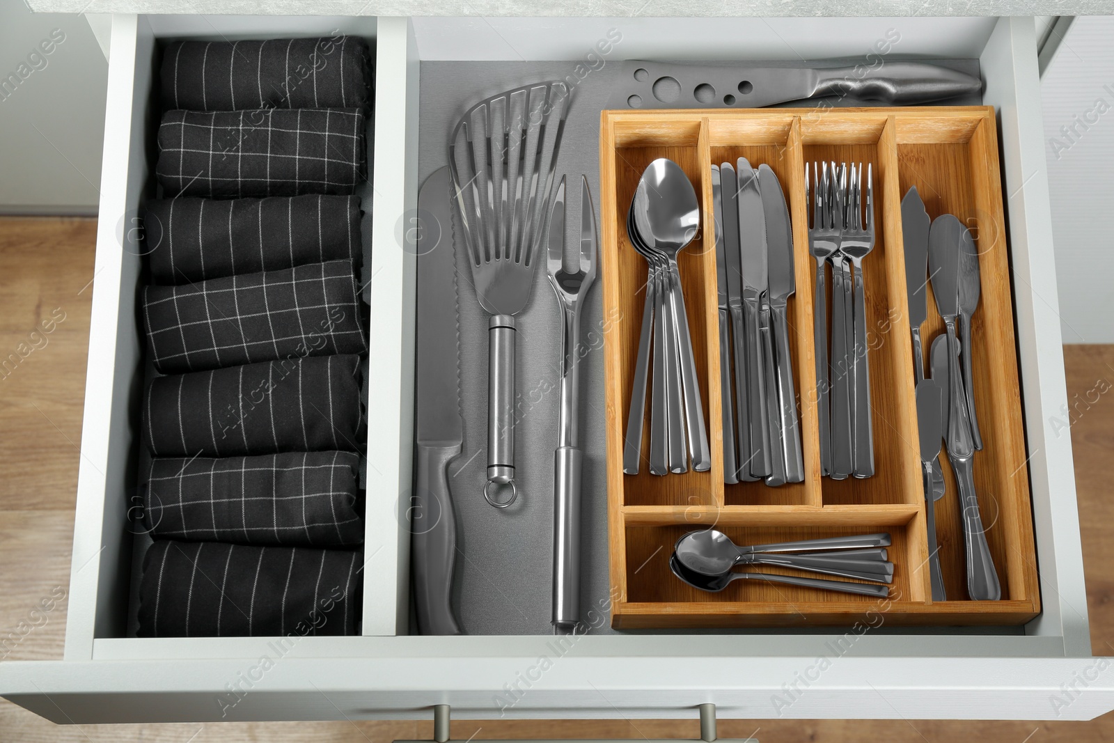 Photo of Open drawer with different utensils and folded towels, top view. Order in kitchen