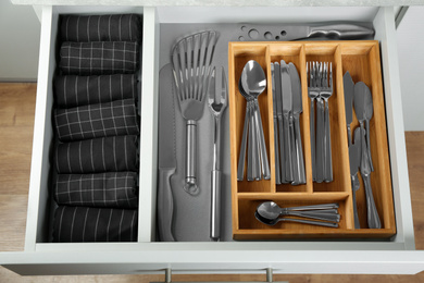 Photo of Open drawer with different utensils and folded towels, top view. Order in kitchen