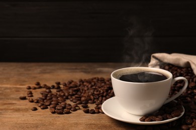 Image of Cup of aromatic hot coffee and beans on wooden table. Space for text