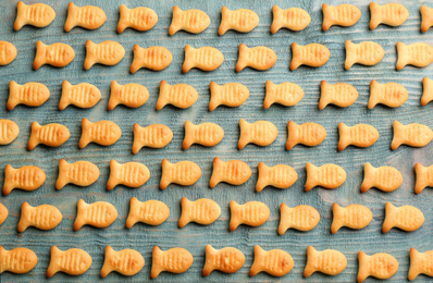 Photo of Delicious goldfish crackers on blue wooden table, flat lay