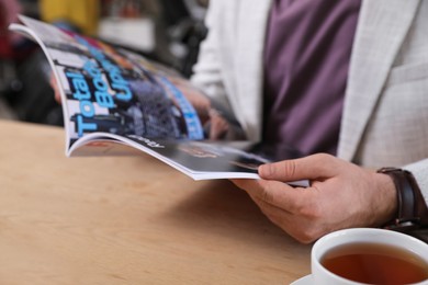 Photo of Young man reading sports magazine at table indoors, closeup