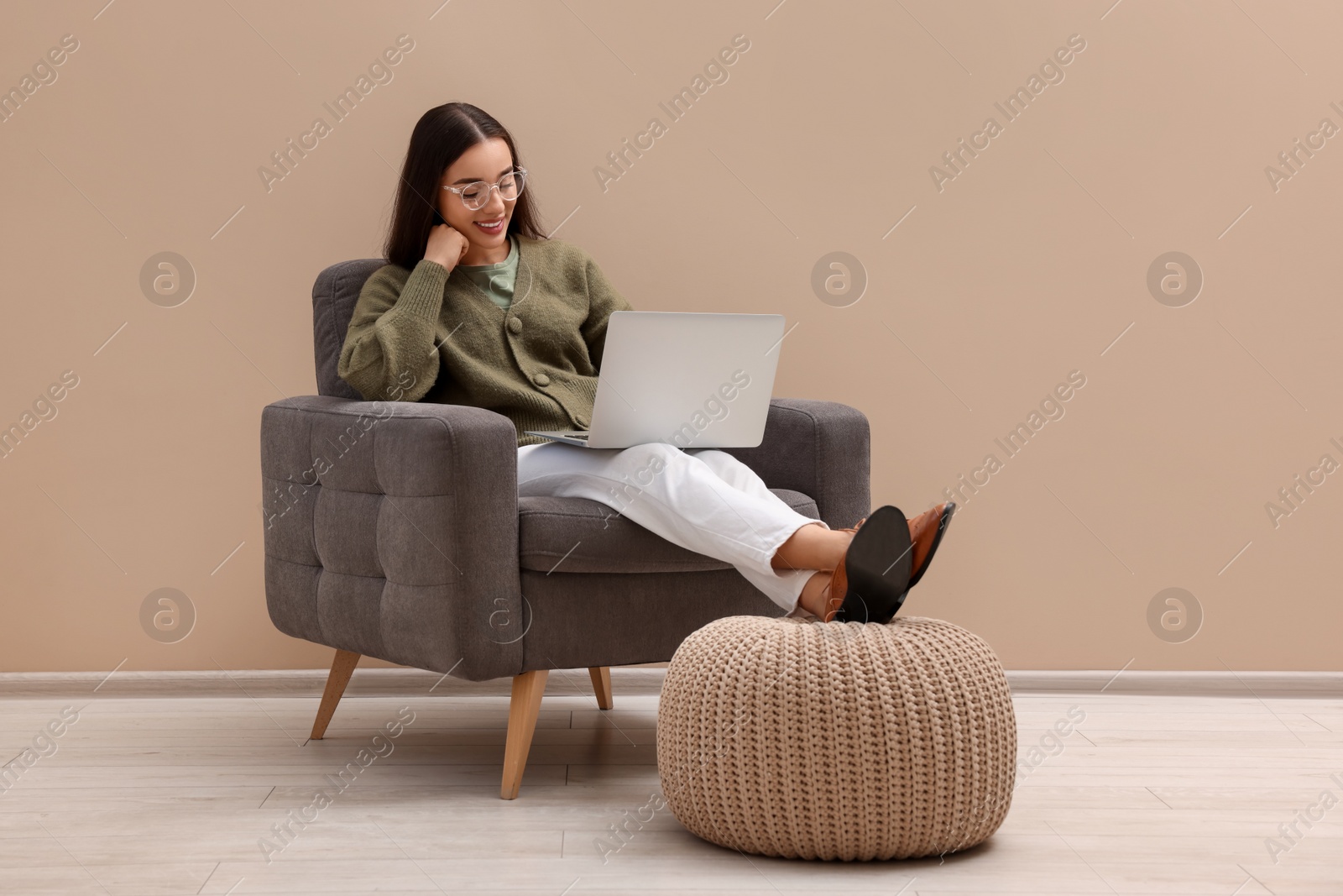 Photo of Beautiful woman with laptop sitting in armchair near beige wall indoors