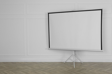 Photo of Blank projection screen near white wall indoors. Space for design