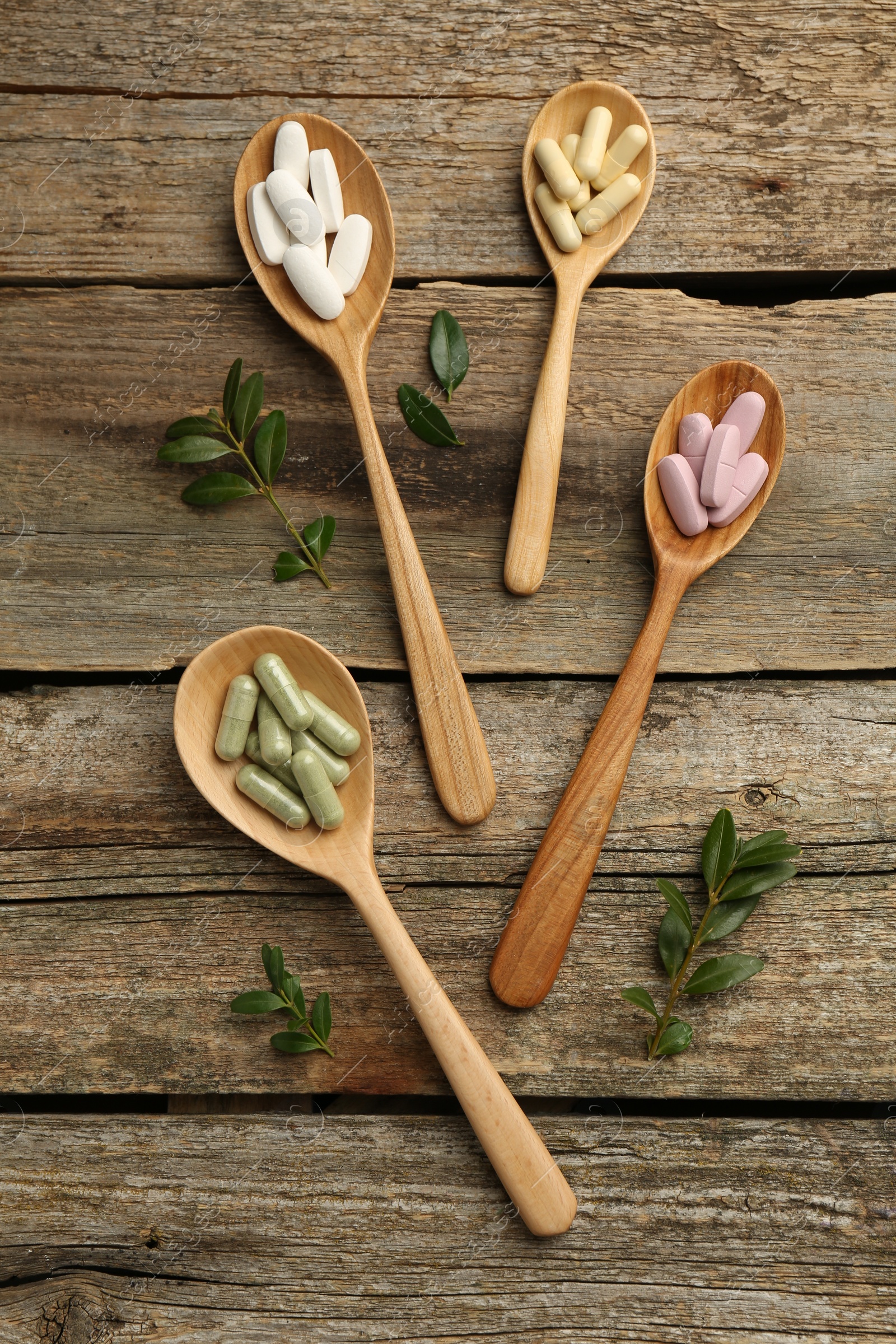 Photo of Vitamin capsules in spoons and leaves on wooden table, flat lay