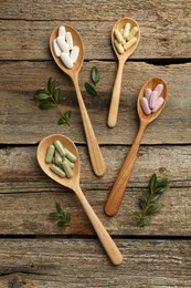 Vitamin capsules in spoons and leaves on wooden table, flat lay