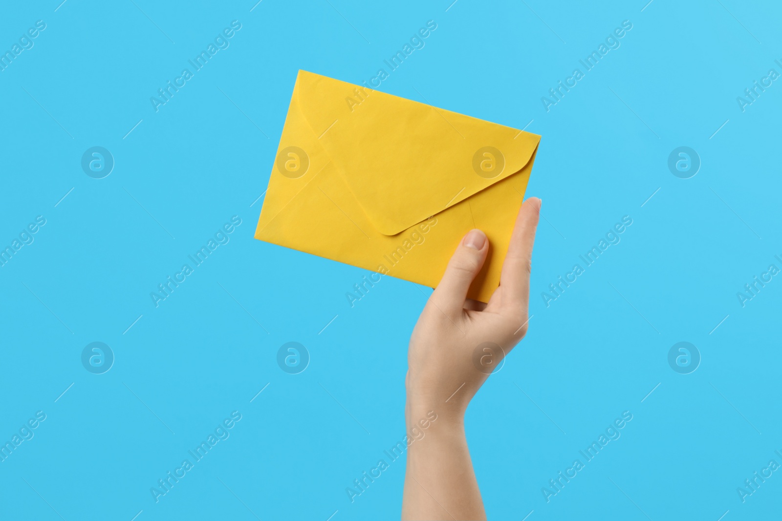 Photo of Woman holding yellow paper envelope on light blue background, closeup