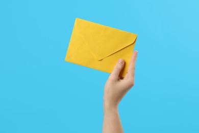 Photo of Woman holding yellow paper envelope on light blue background, closeup