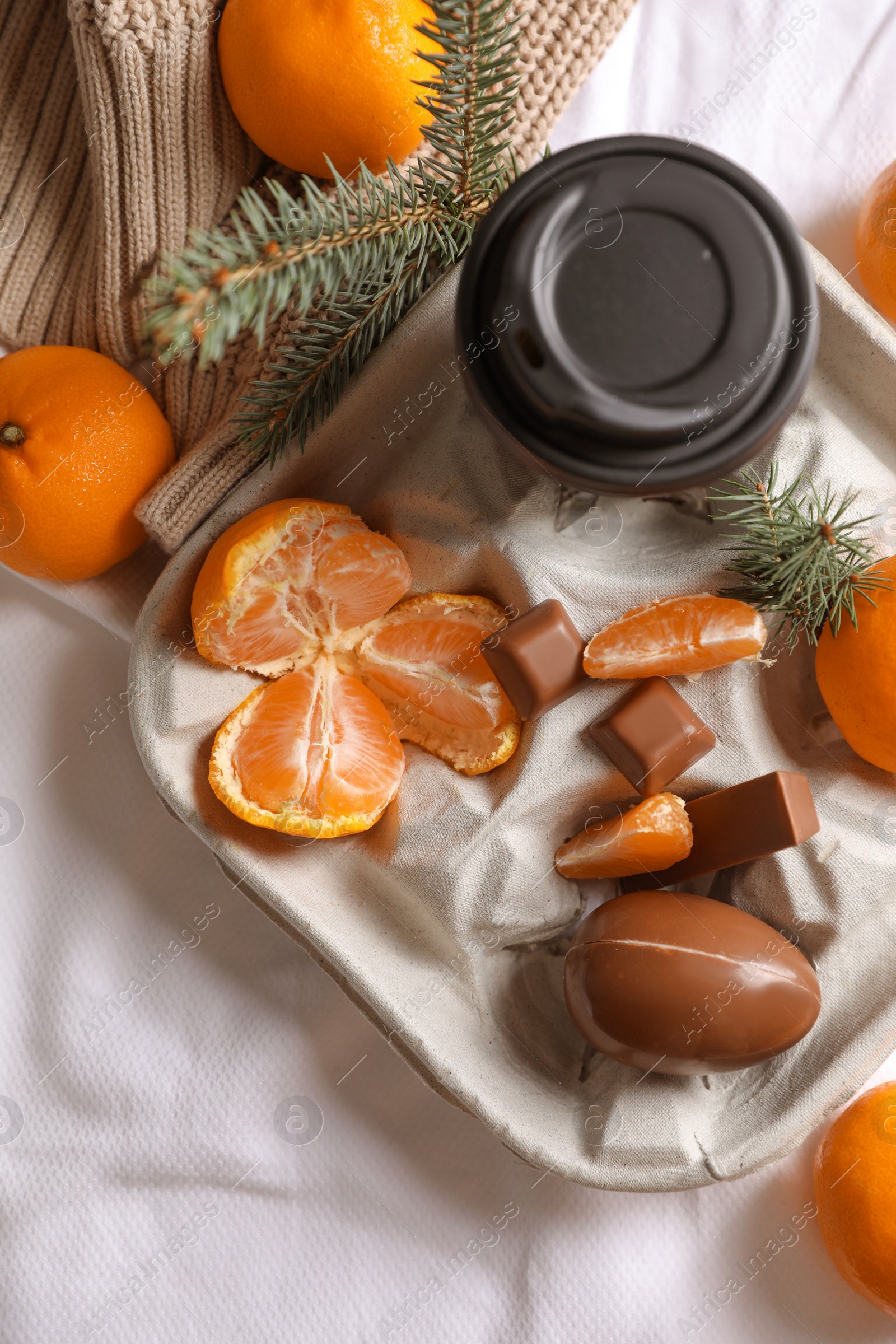 Photo of Delicious ripe tangerines, cup with drink and chocolates on white bedsheet, flat lay