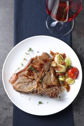 Delicious fried beef meat, vegetables and wine on grey table, top view