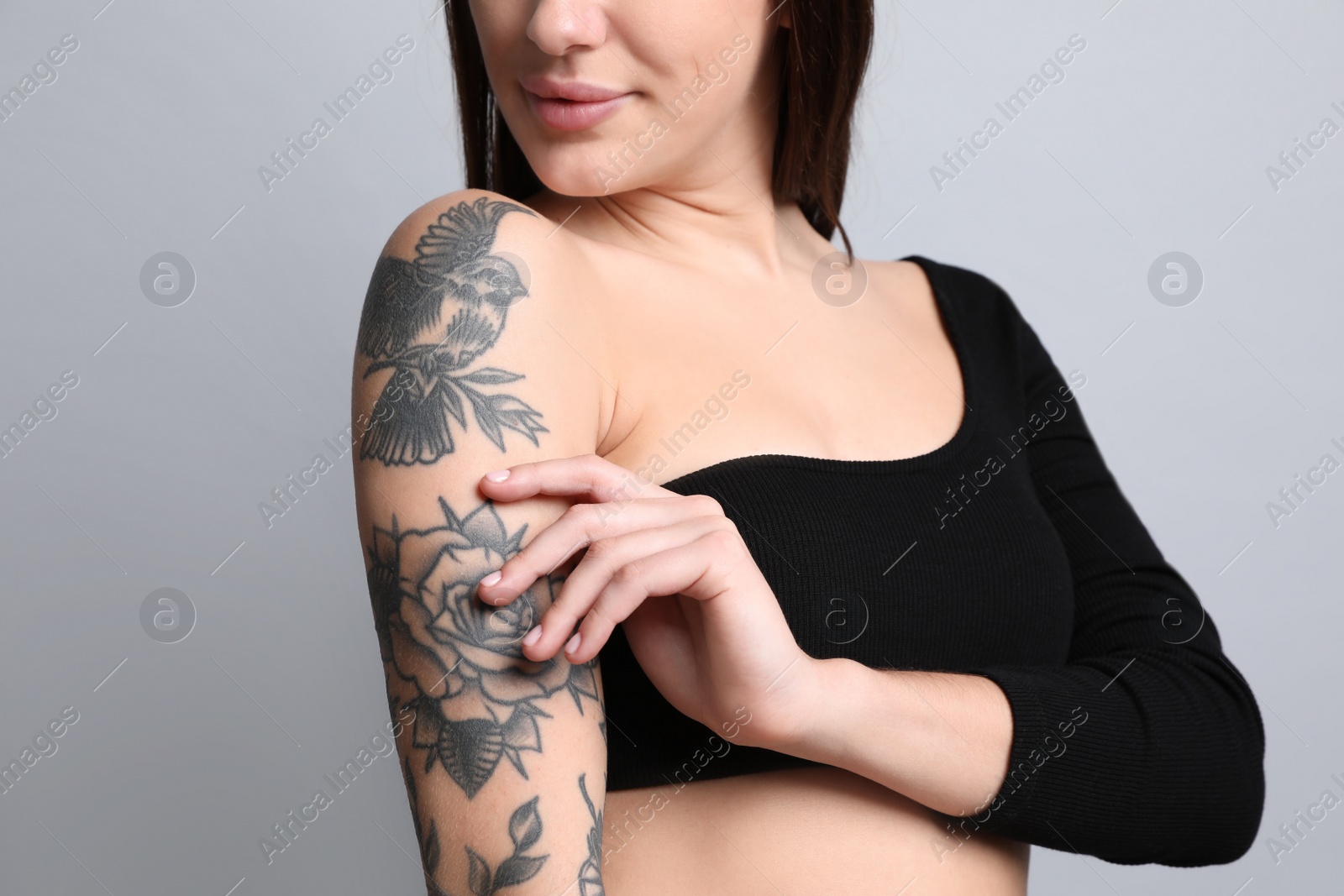 Photo of Beautiful woman with tattoos on arm against grey background, closeup